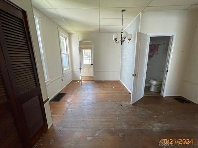 unfurnished dining area featuring visible vents, a chandelier, a drop ceiling, and wood finished floors