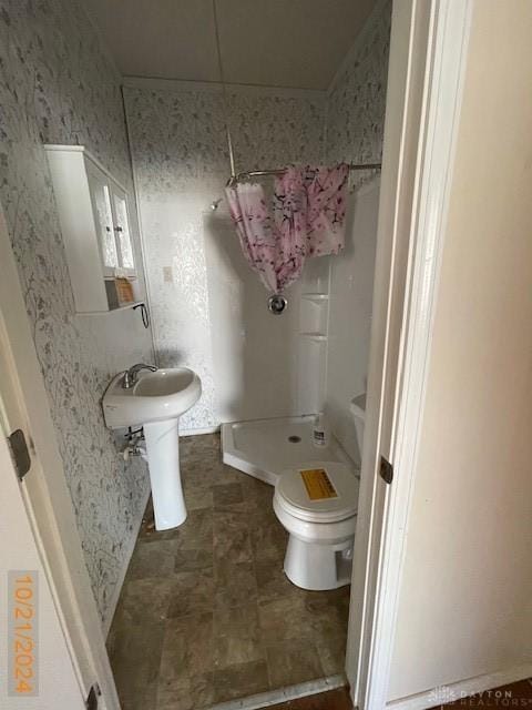 full bathroom featuring toilet, wallpapered walls, a shower stall, and a sink