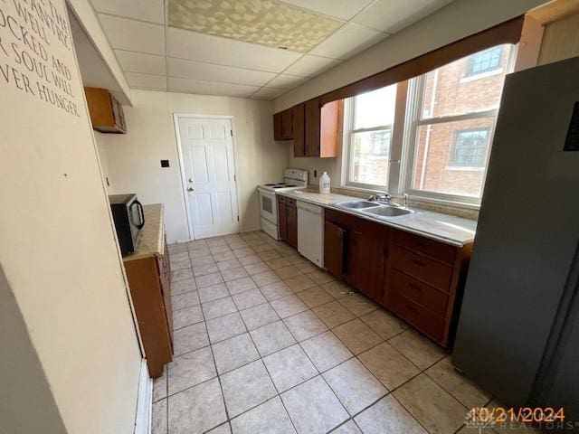 kitchen with light tile patterned floors, a drop ceiling, white appliances, a sink, and light countertops