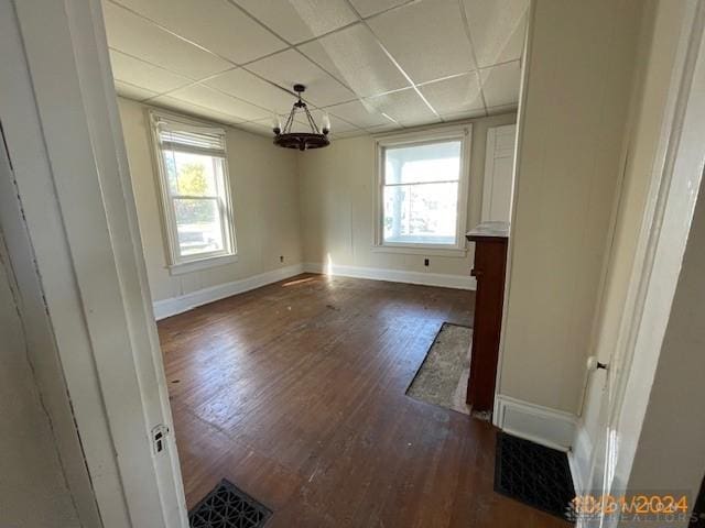 unfurnished dining area featuring a paneled ceiling, plenty of natural light, wood finished floors, and visible vents