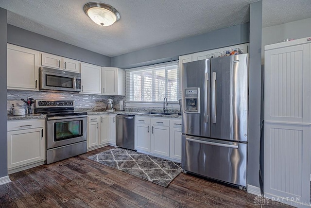 kitchen with dark wood finished floors, white cabinetry, stainless steel appliances, and a sink