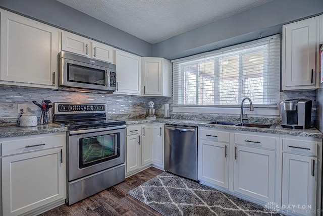 kitchen with dark wood finished floors, appliances with stainless steel finishes, a sink, and white cabinetry