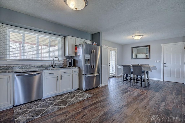 kitchen with stone countertops, dark wood-type flooring, stainless steel appliances, white cabinetry, and a sink