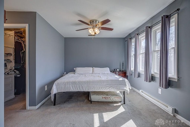 carpeted bedroom with a ceiling fan, baseboards, a closet, baseboard heating, and a walk in closet