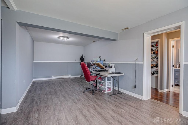 office space with a baseboard heating unit, wood finished floors, visible vents, and baseboards