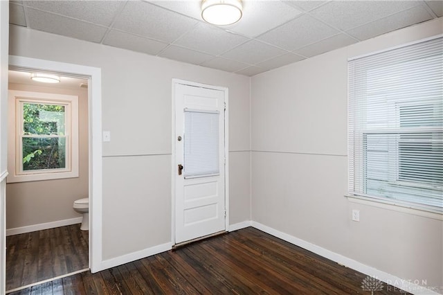 unfurnished room with a drop ceiling, dark wood finished floors, and baseboards