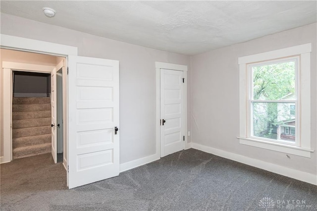 unfurnished bedroom featuring dark carpet and baseboards