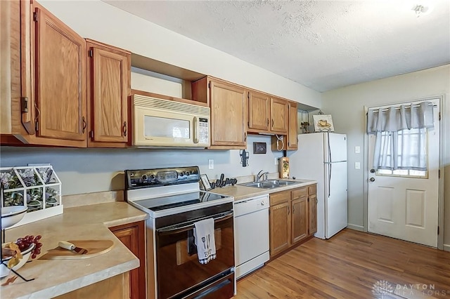 kitchen with white appliances, light countertops, a sink, and light wood finished floors