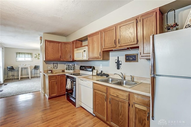 kitchen with white appliances, brown cabinets, light countertops, light wood-style floors, and a sink