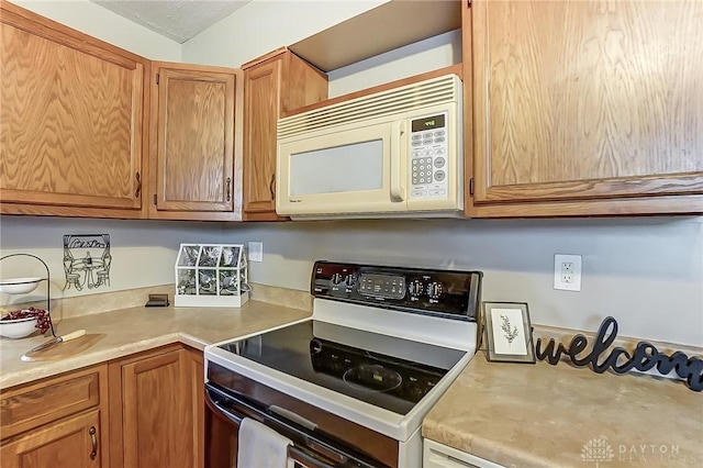 kitchen featuring brown cabinetry, range with electric cooktop, light countertops, and white microwave