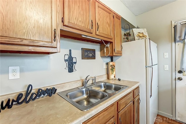 kitchen featuring brown cabinetry, freestanding refrigerator, light countertops, and a sink