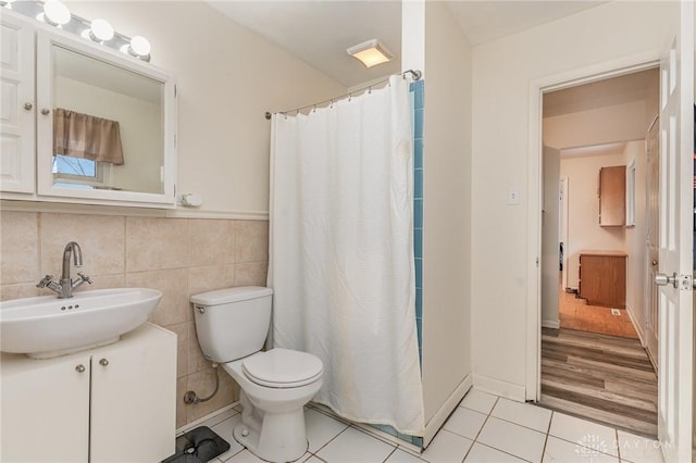 full bath featuring curtained shower, toilet, a sink, tile walls, and tile patterned floors