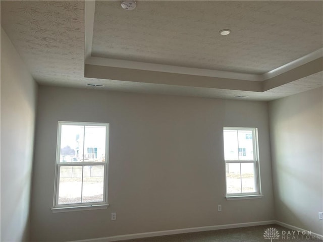 carpeted empty room featuring a tray ceiling, visible vents, a textured ceiling, and baseboards