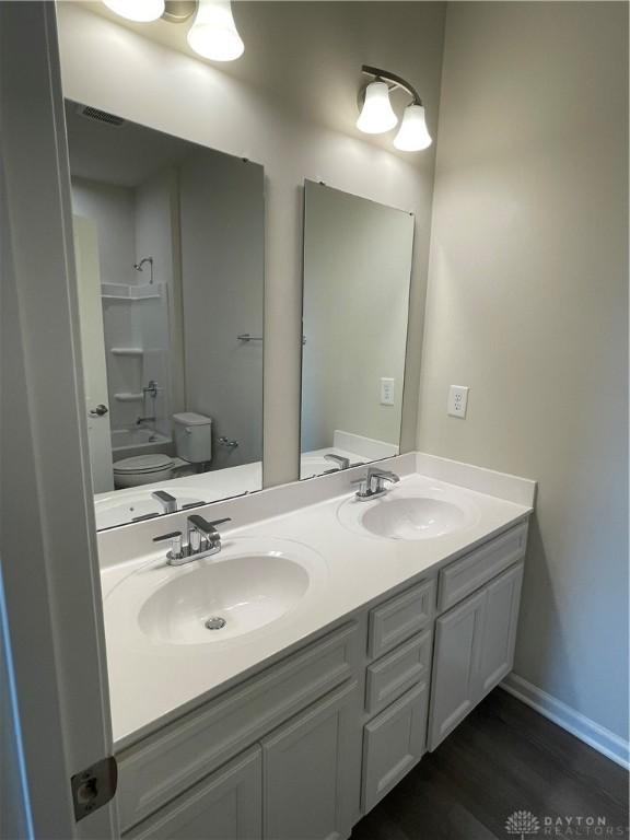 bathroom featuring washtub / shower combination, a sink, toilet, and double vanity