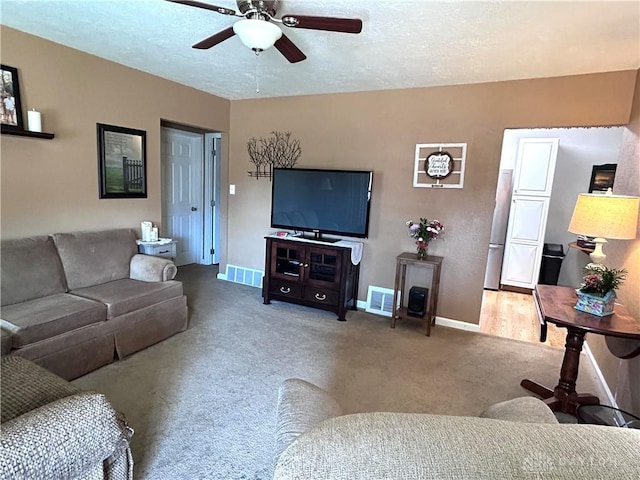 carpeted living room with baseboards, visible vents, ceiling fan, and a textured ceiling