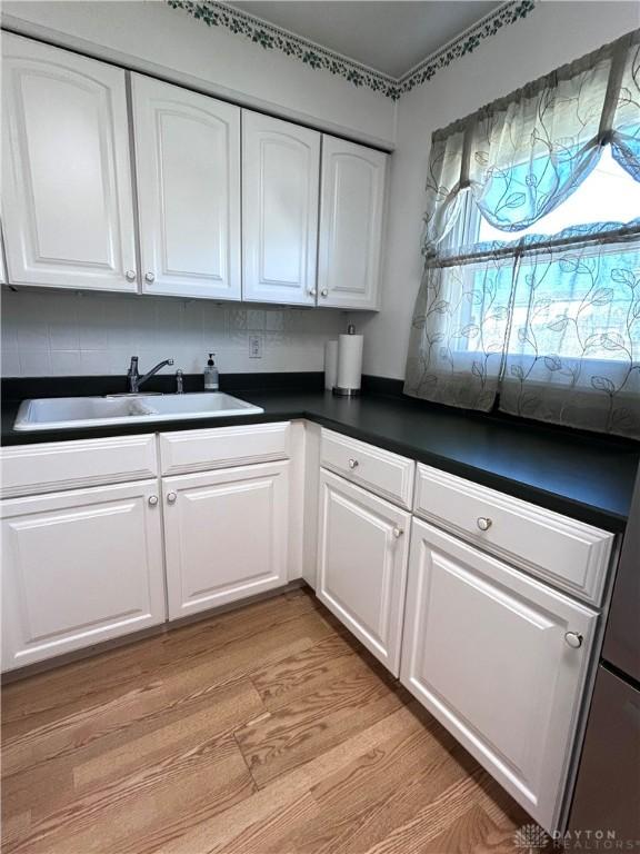 kitchen featuring dark countertops, white cabinets, a sink, and light wood-style flooring