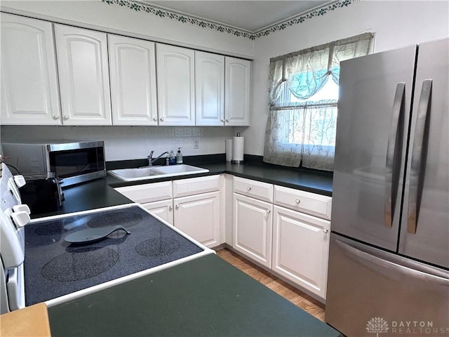 kitchen featuring dark countertops, light wood-style flooring, appliances with stainless steel finishes, white cabinets, and a sink