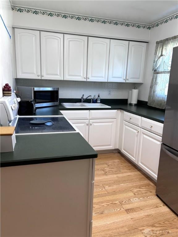 kitchen featuring appliances with stainless steel finishes, dark countertops, a sink, and white cabinets