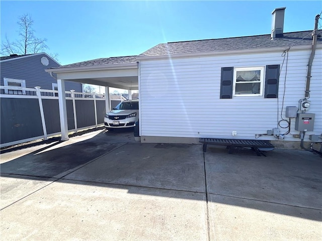 view of property exterior featuring driveway, an attached carport, roof with shingles, and fence