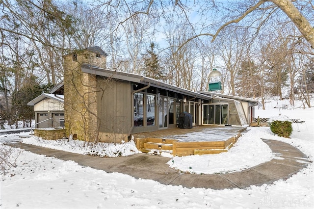 snow covered back of property featuring a chimney and a wooden deck