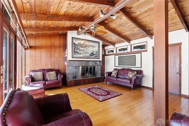 living area with ceiling fan, vaulted ceiling with beams, hardwood / wood-style flooring, wood ceiling, and a glass covered fireplace