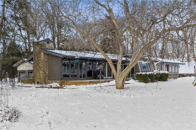 snow covered back of property with a sunroom