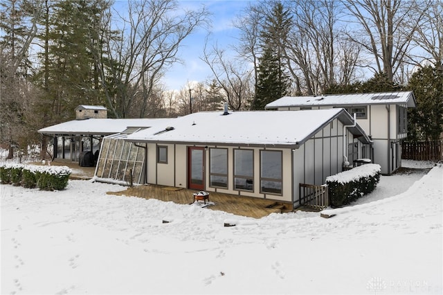 snow covered house with board and batten siding and a sunroom