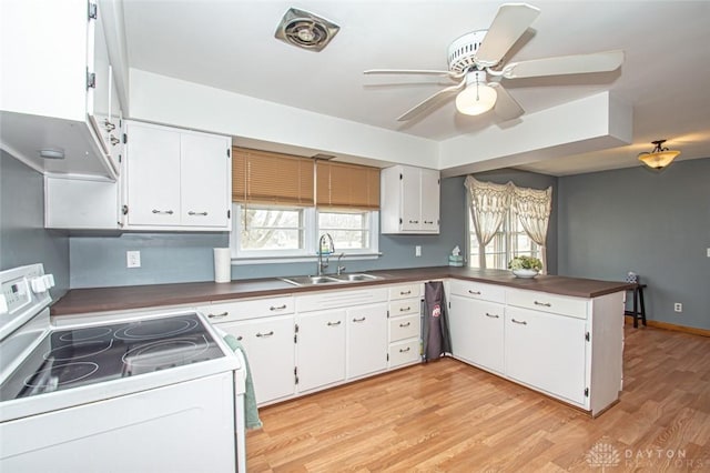 kitchen with light wood finished floors, dark countertops, a peninsula, white electric range, and a sink