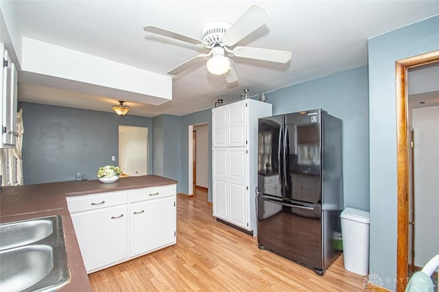 kitchen with freestanding refrigerator, white cabinets, a sink, ceiling fan, and light wood-type flooring