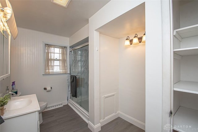 bathroom with toilet, a stall shower, baseboard heating, and wood finished floors