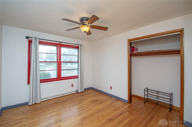 unfurnished bedroom with a closet, a baseboard heating unit, light wood-style floors, a ceiling fan, and baseboards