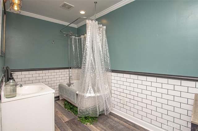 full bath featuring wood finished floors, visible vents, tile walls, ornamental molding, and wainscoting