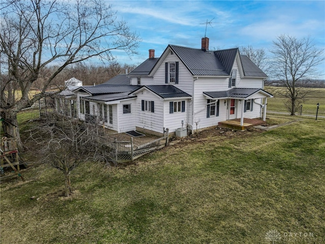 back of house featuring a chimney, a lawn, a standing seam roof, central AC, and metal roof