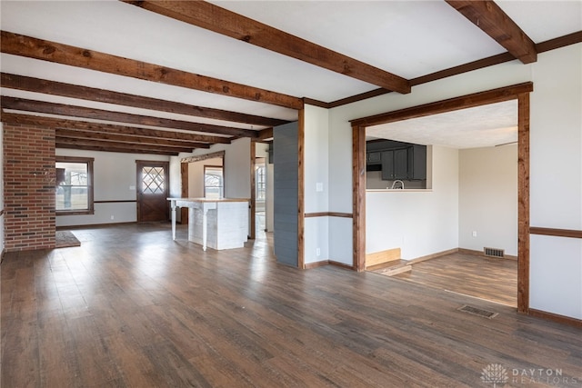 unfurnished living room featuring beam ceiling, dark wood-style flooring, visible vents, and baseboards