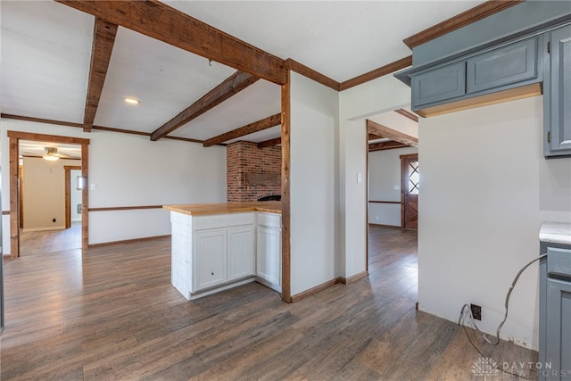 kitchen featuring baseboards, dark wood-type flooring, light countertops, a brick fireplace, and beam ceiling