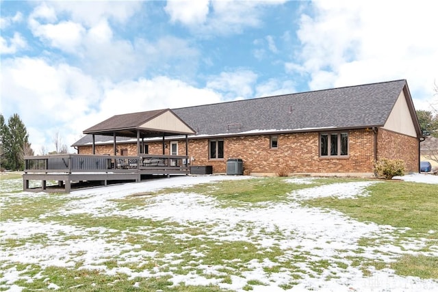 snow covered rear of property featuring brick siding, roof with shingles, a gazebo, central AC unit, and a deck