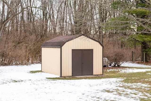 snow covered structure featuring a storage shed and an outbuilding