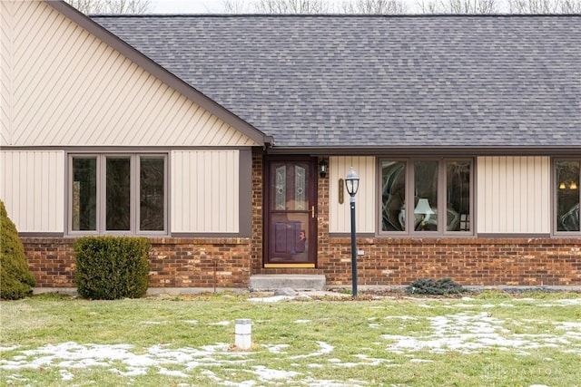 doorway to property featuring a shingled roof and brick siding