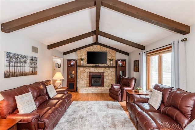 living room with visible vents, vaulted ceiling with beams, a stone fireplace, and wood finished floors