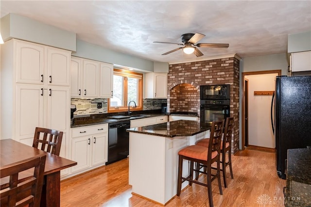 kitchen featuring light wood-style flooring, a kitchen breakfast bar, backsplash, dark stone counters, and black appliances