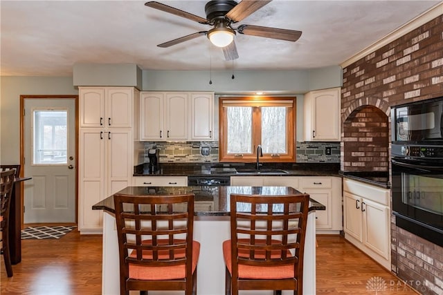 kitchen with a healthy amount of sunlight, a sink, black appliances, and wood finished floors