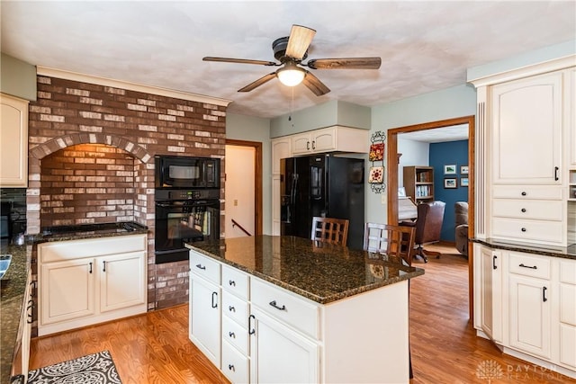 kitchen with light wood finished floors, a kitchen island, ceiling fan, dark stone counters, and black appliances