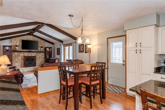 dining space featuring light wood-style floors, plenty of natural light, vaulted ceiling with beams, and a fireplace