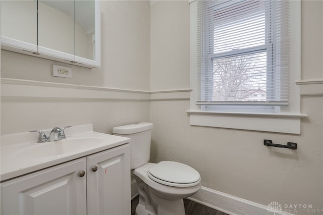 half bath with wood finished floors, vanity, toilet, and baseboards