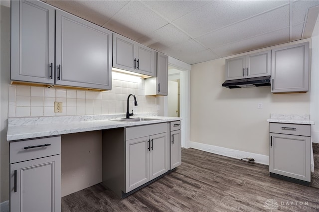 kitchen featuring under cabinet range hood, dark wood-style flooring, a sink, gray cabinets, and tasteful backsplash