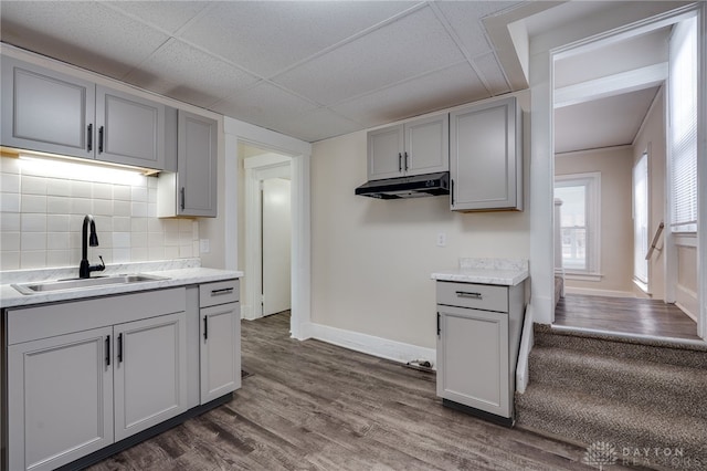 kitchen with backsplash, gray cabinetry, dark wood-type flooring, a sink, and under cabinet range hood