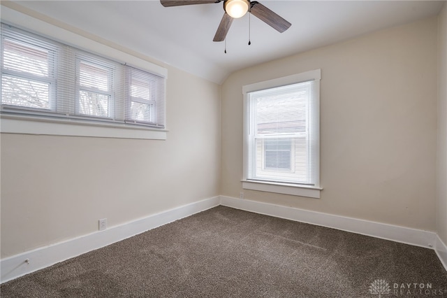 spare room featuring a wealth of natural light, baseboards, vaulted ceiling, and dark colored carpet