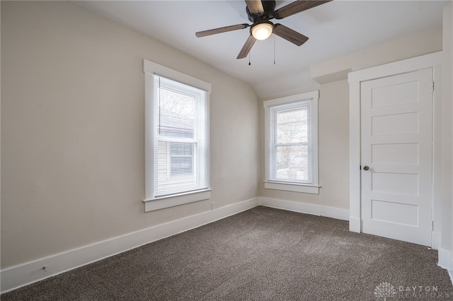 spare room with lofted ceiling, dark carpet, baseboards, and ceiling fan