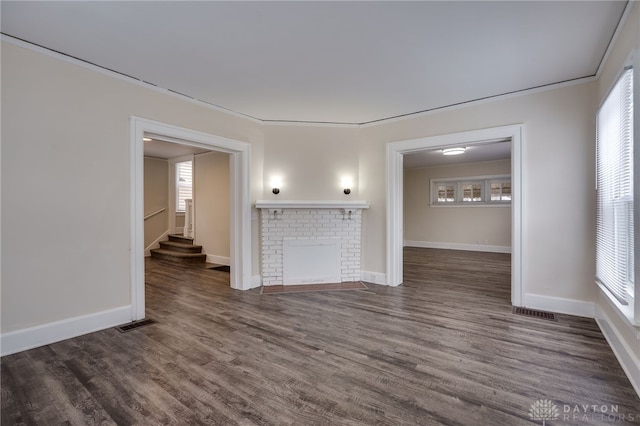 empty room with a brick fireplace, visible vents, baseboards, and dark wood finished floors