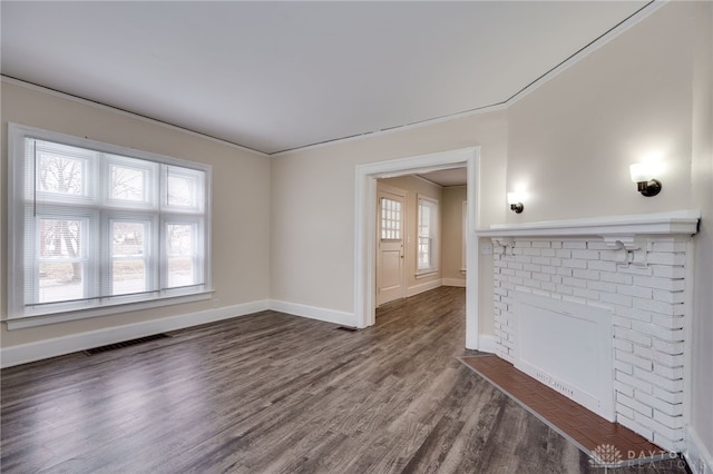 unfurnished living room with a brick fireplace, visible vents, baseboards, and wood finished floors